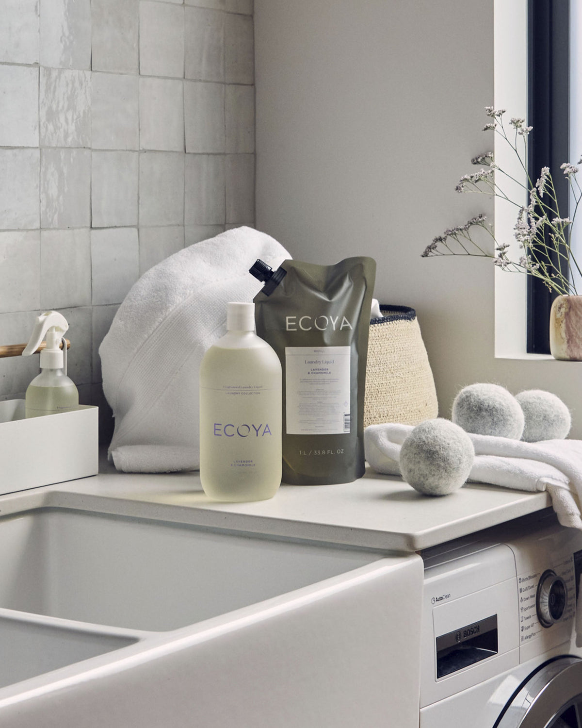 Ecoya laundry liquid, refill pouch and wool dryer balls styled on a laundry bench beside a butler sink