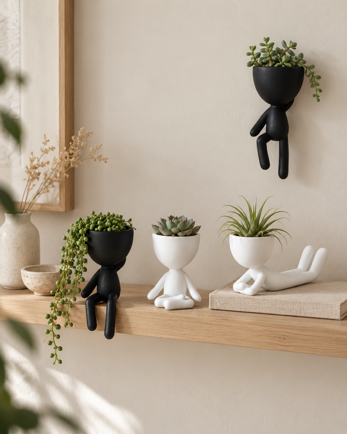 Four egg head planters styled on a light oak floating shelf: black wall planter hung above, black shelf planter with legs dangling over the edge, white desk planter seated cross-legged and white yoga planter reclining, planted with faux succulents and air plants