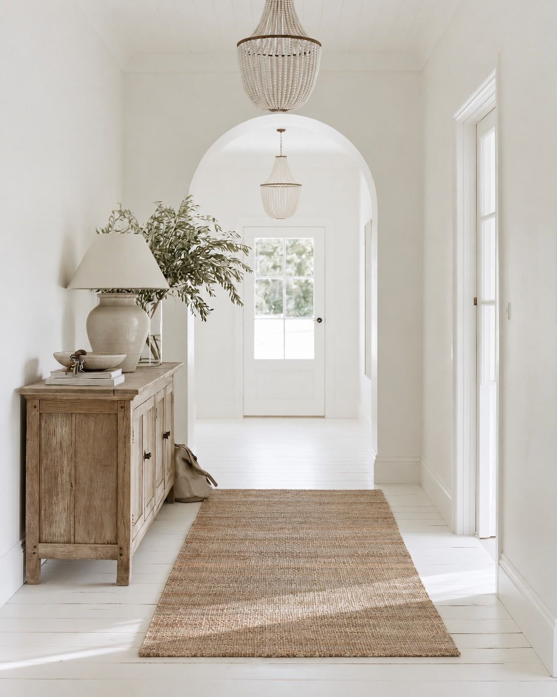 Eka Jute Rug as a runner beside a rustic timber sideboard in a white entry hall with an arched doorway