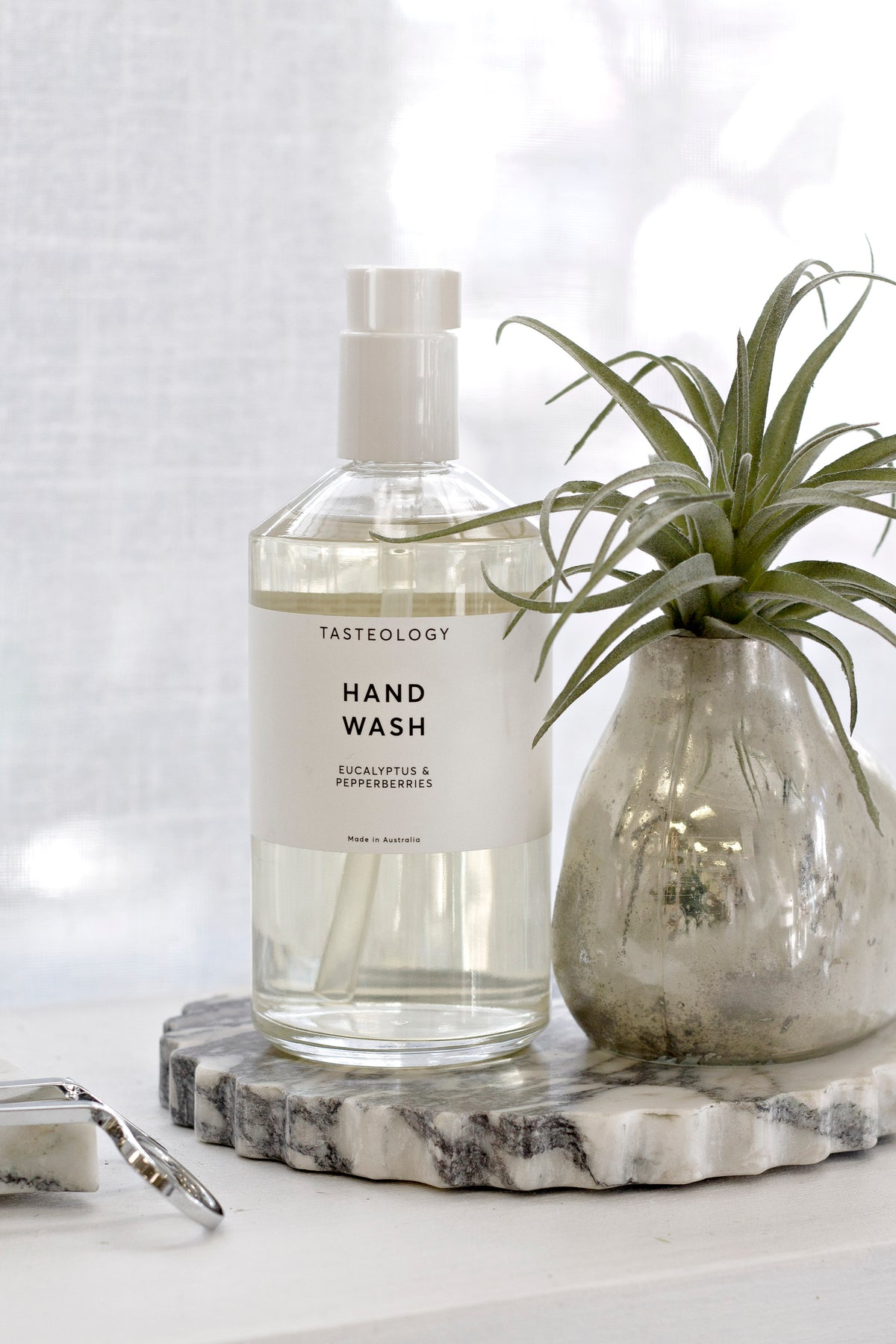 Calacatta marble petal-edge tray styled with Tasteology hand wash and a small glass vase with air plant