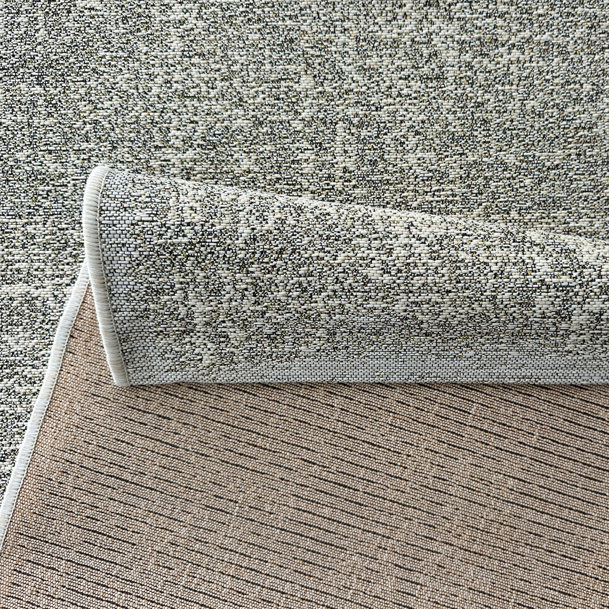 Folded corner of the outdoor rug showing the flat weave and textured backing