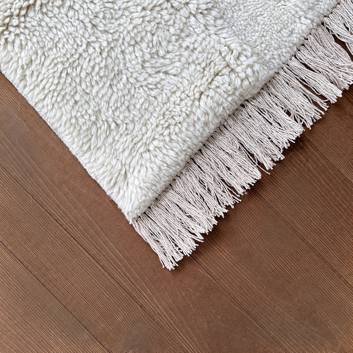 Corner of the ivory wool rug with its fringe on a dark timber floor