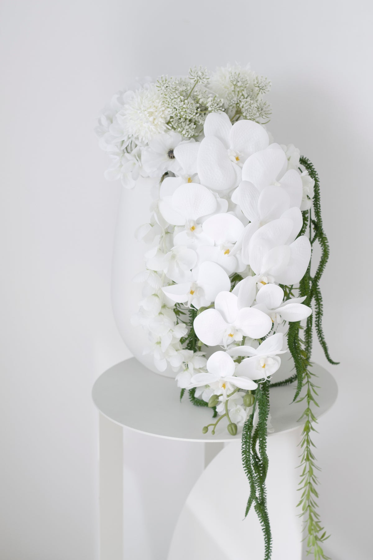 White orchid and hydrangea bouquet in a tall white vase on a round side table
