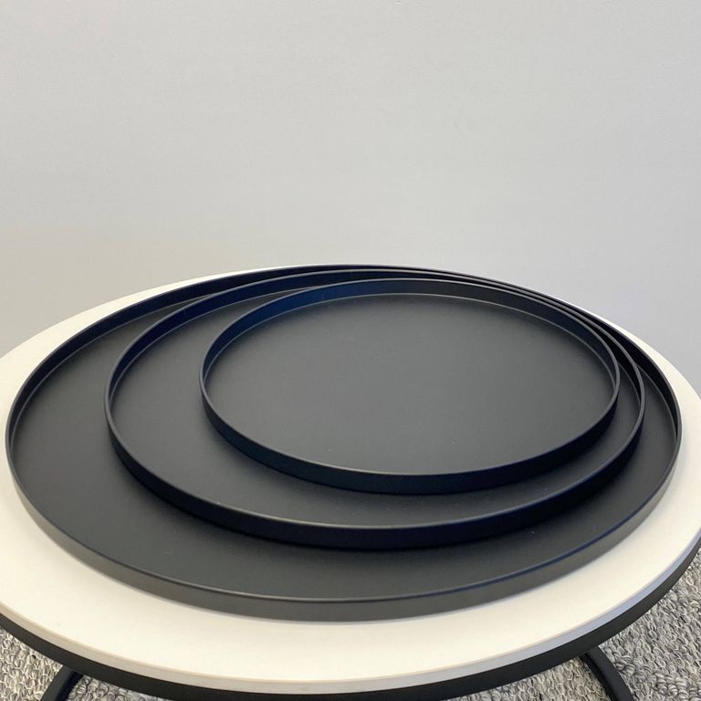 Three black Bianca trays nested by size on a round white side table against a grey wall