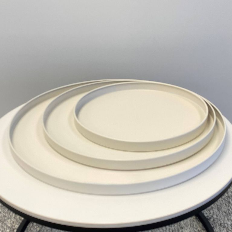Three beige Bianca trays nested by size on a round white side table