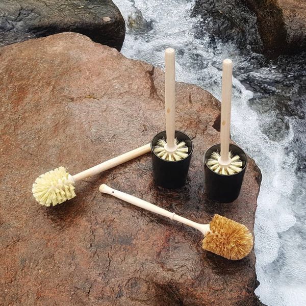 Toilet brushes with timber handles in black and white holders on a rock by rushing water