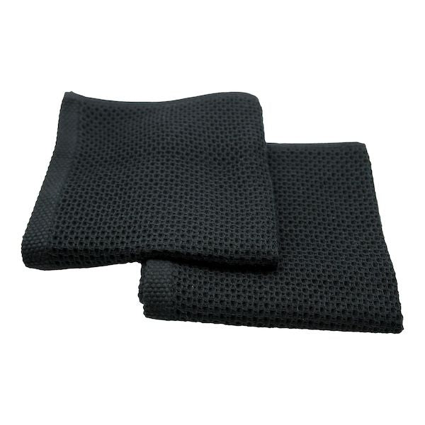 Two black waffle-weave cotton wash cloths, folded, on white