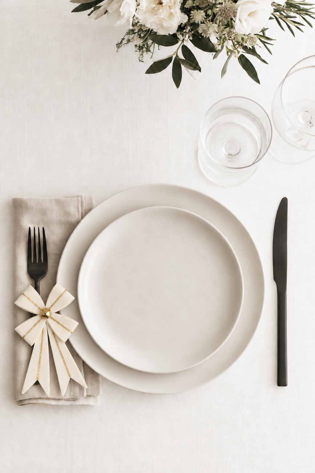 Ivory and gold felt bow on a linen napkin beside a black fork in a white Christmas table setting