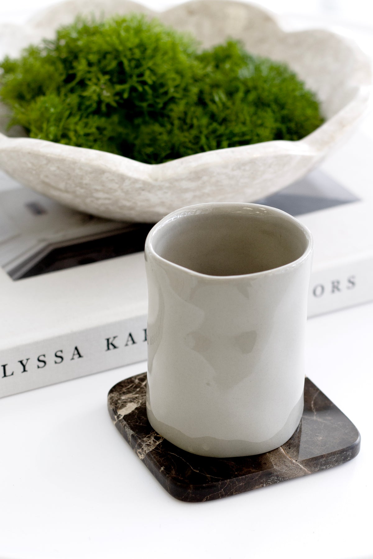 Tumbler on a dark marble coaster in front of a scalloped bowl of moss on books