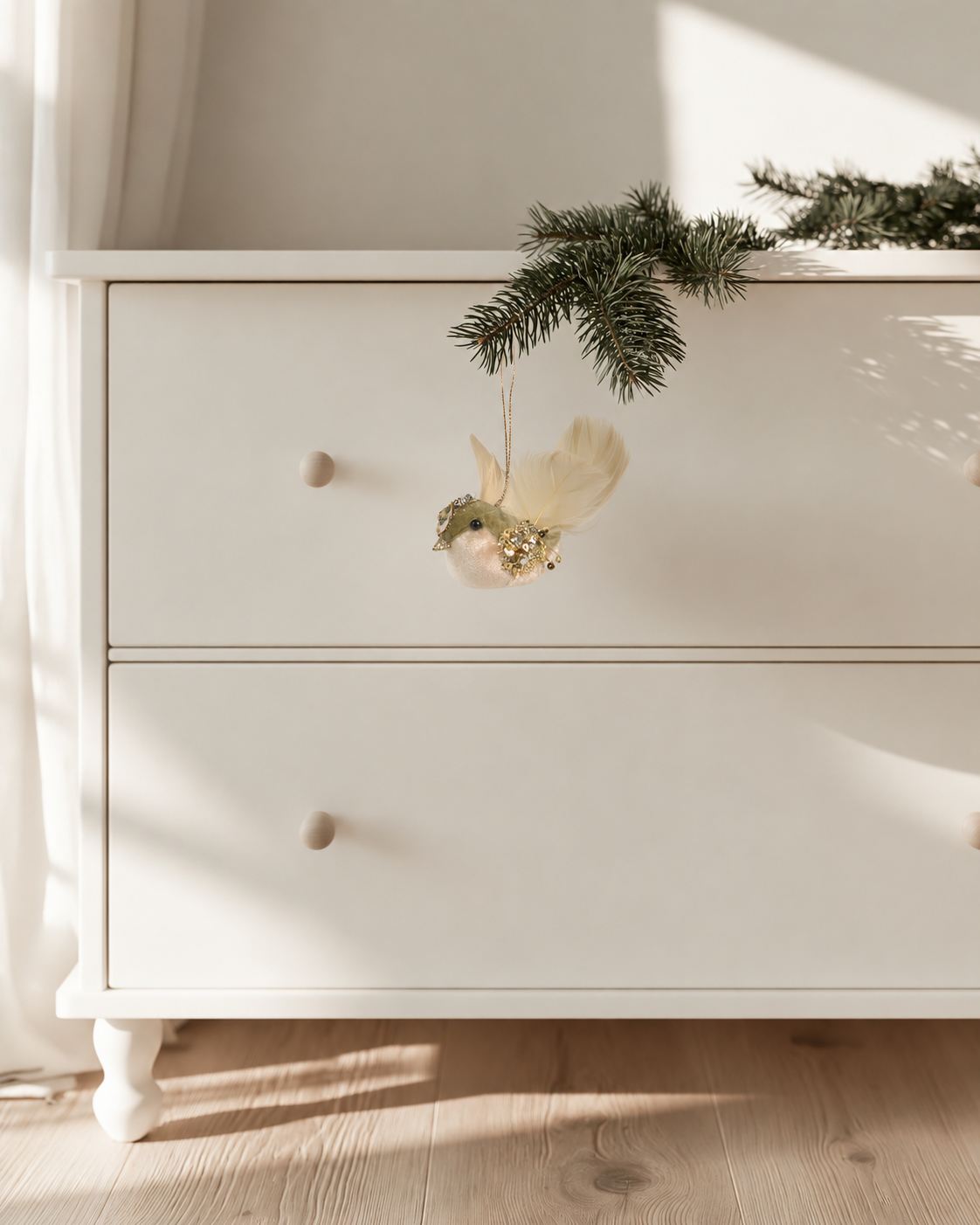 Forest Finch chick hanging decoration on a pine branch draped over a white dresser