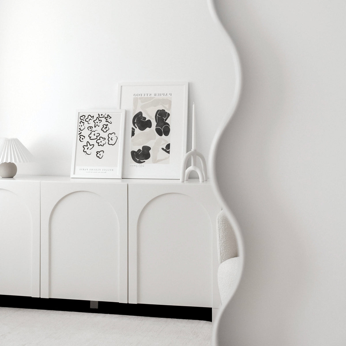 Fleurs and Belle Femme prints on a white sideboard beside a wavy mirror