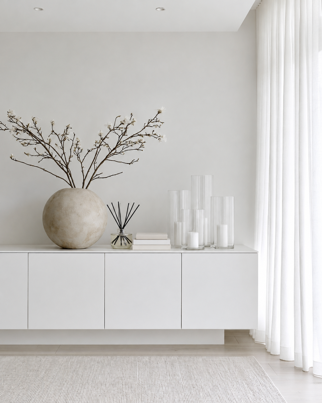 Ecoya reed diffuser beside a stone vase and clear glass cylinder vases with candles on a white sideboard