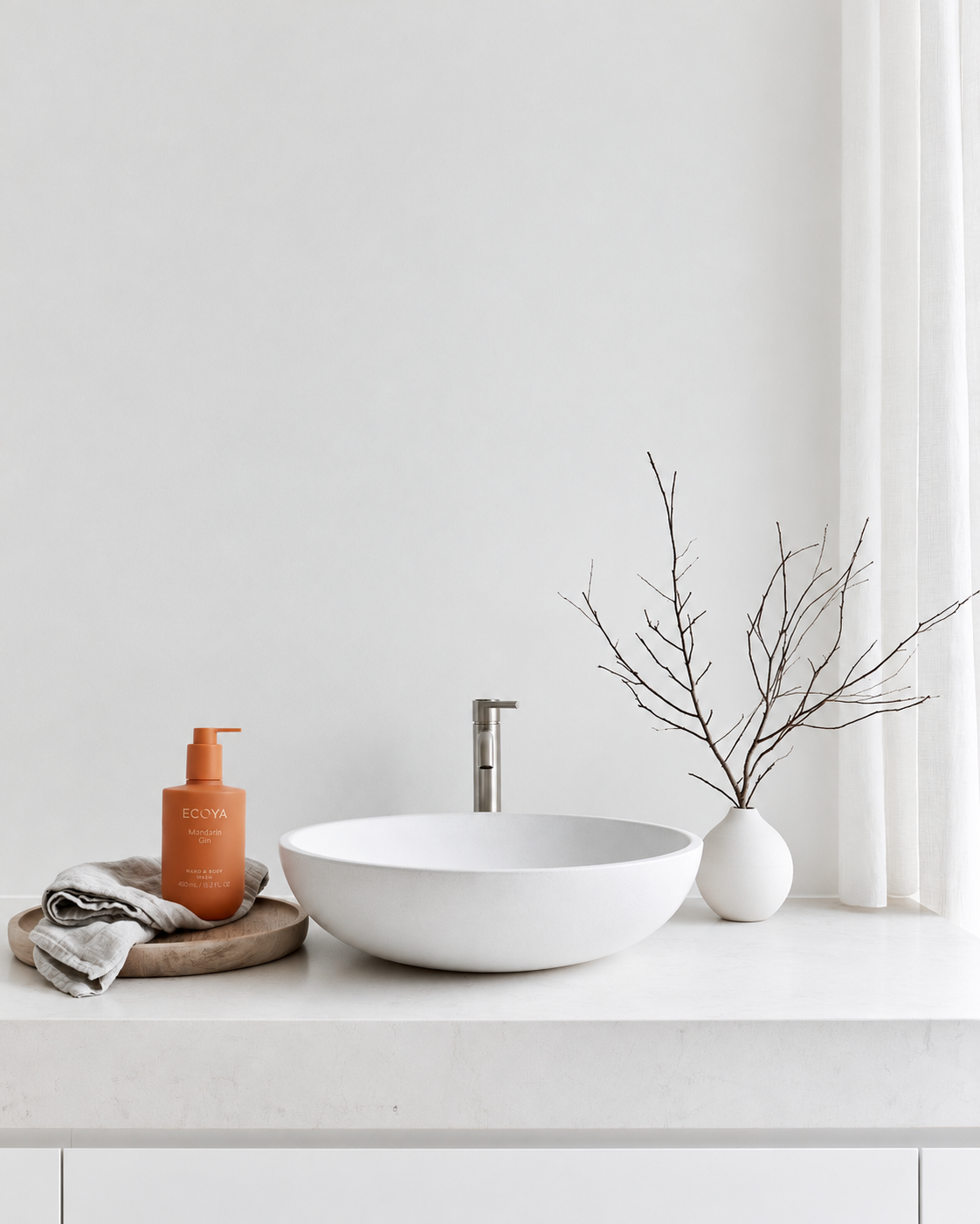 Ecoya Mandarin Gin hand and body wash in an orange pump bottle on a timber tray beside a white basin