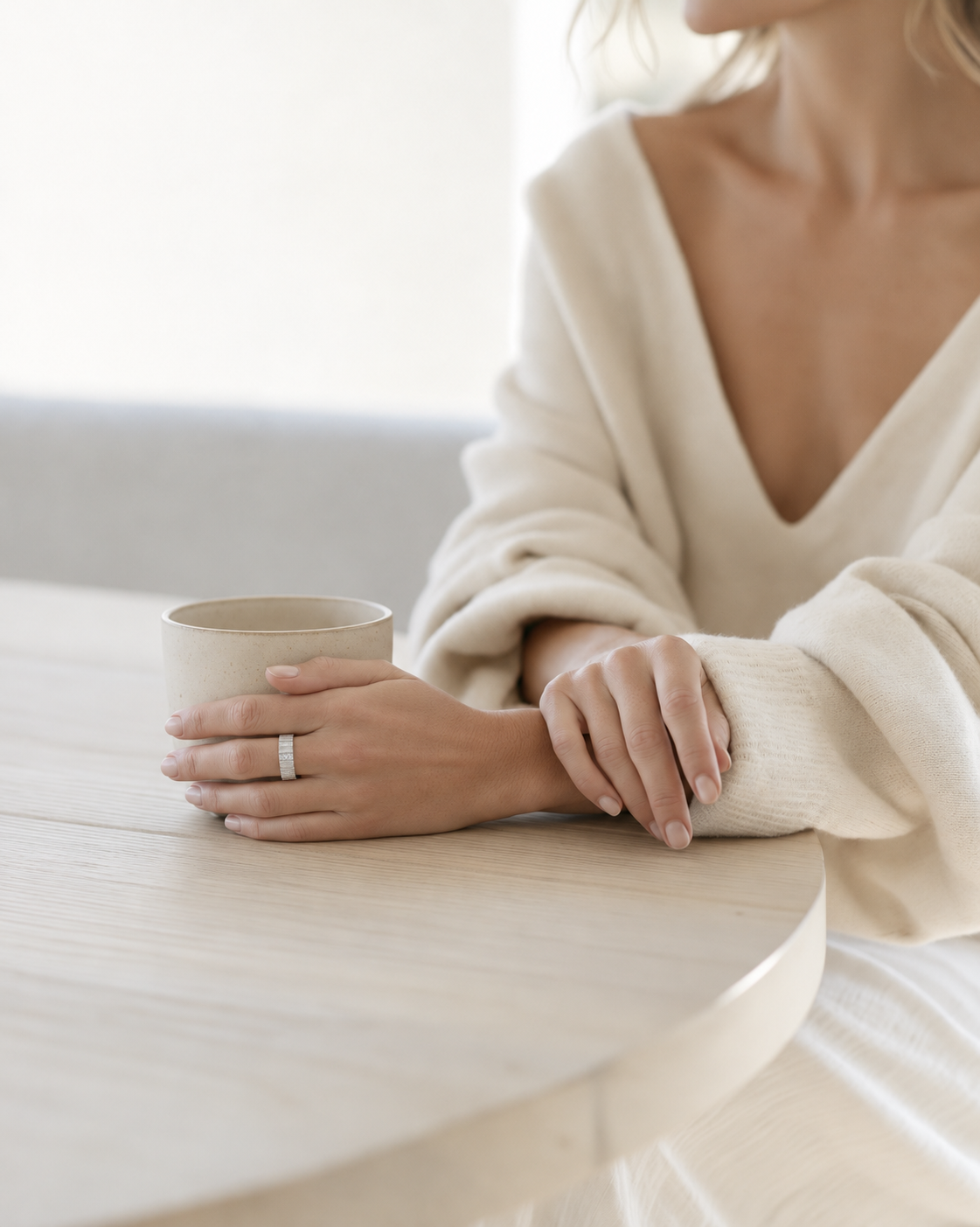 Woman at a white table wearing the Federation Impressions Ring in matte silver