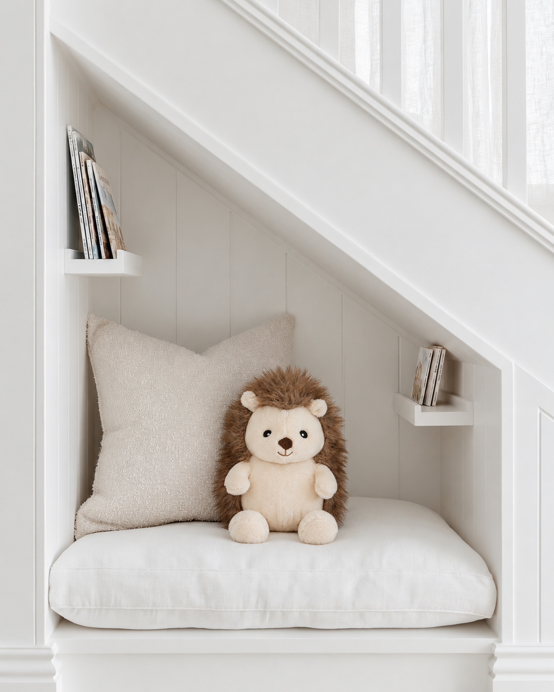 Hugo the Hedgehog soft toy by Lily & George sitting on a cushioned reading nook under the stairs