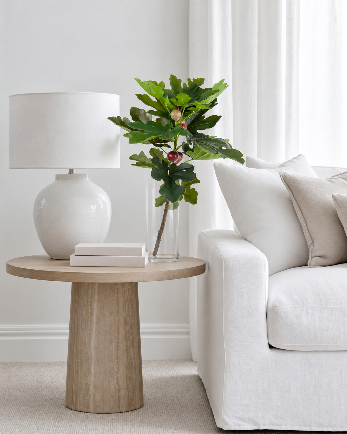 Fig leaf spray with figs in a clear glass vase on a round side table beside a white sofa