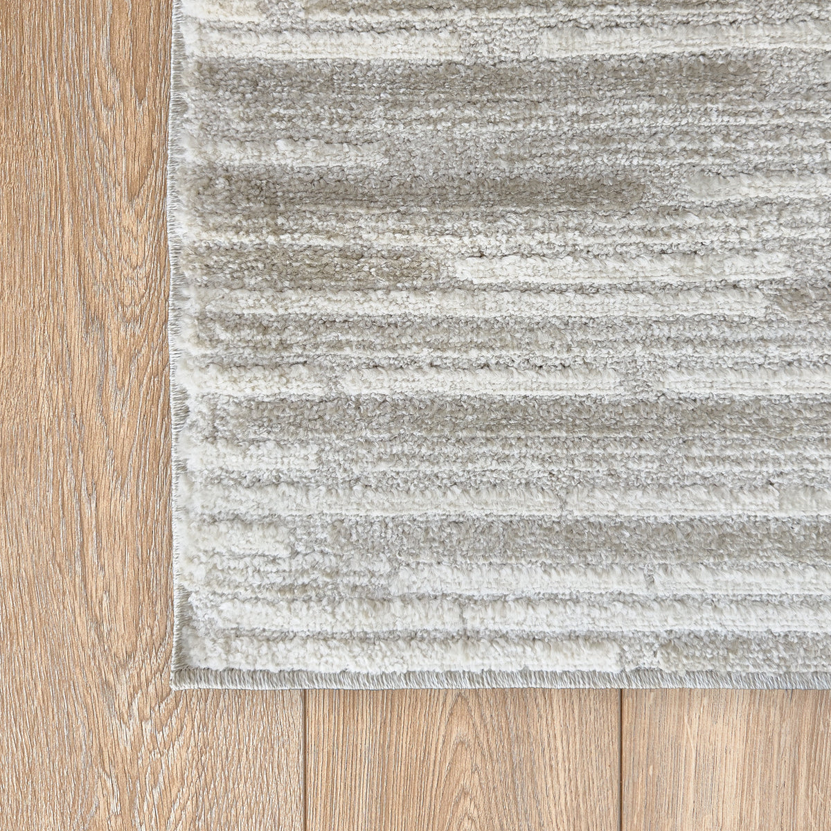 Corner of the beige textured rug on a light timber floor