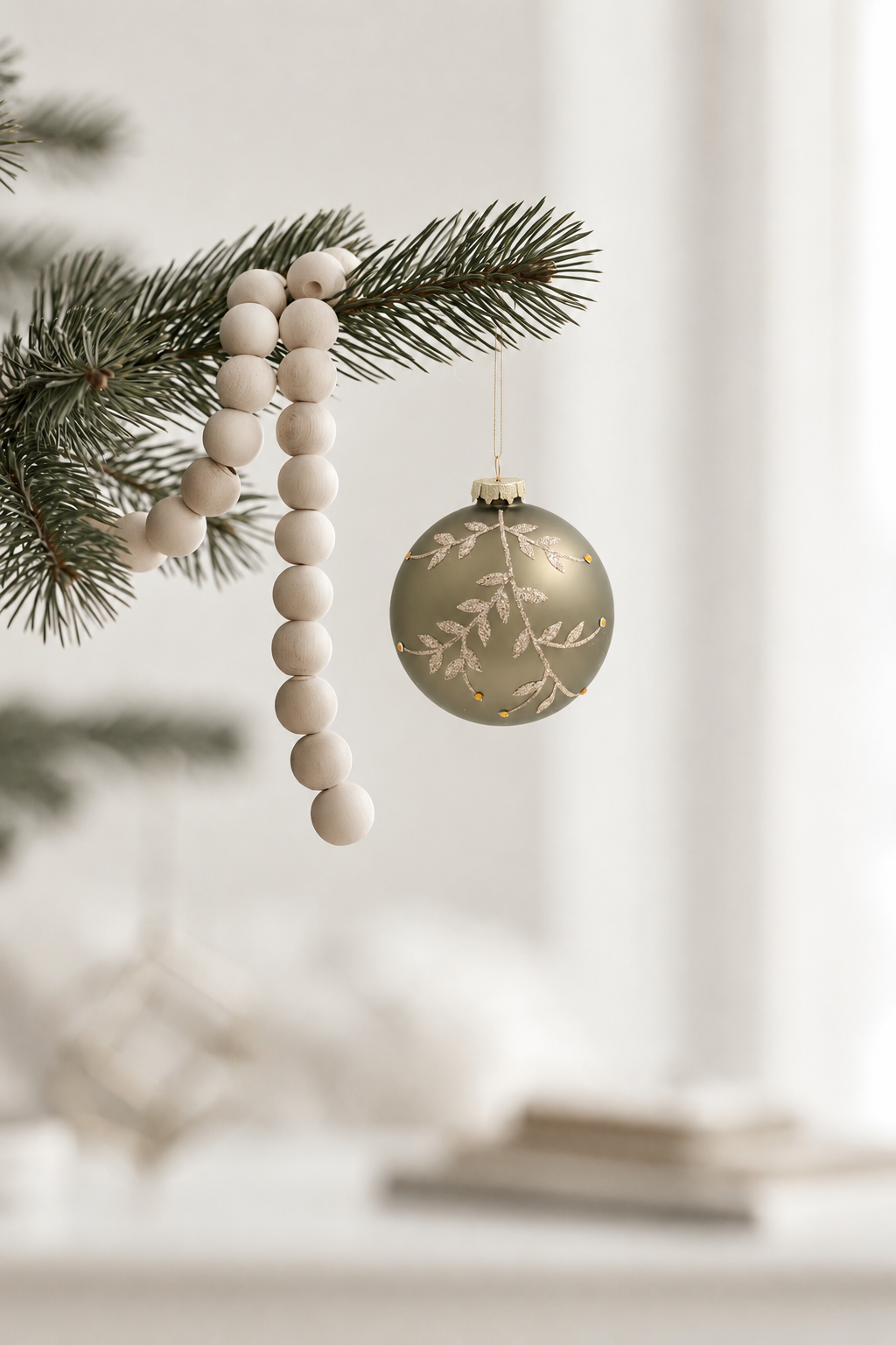 Gilded Vine Glass Bauble in sage and champagne 10cm hanging from a pine branch beside a wooden bead garland