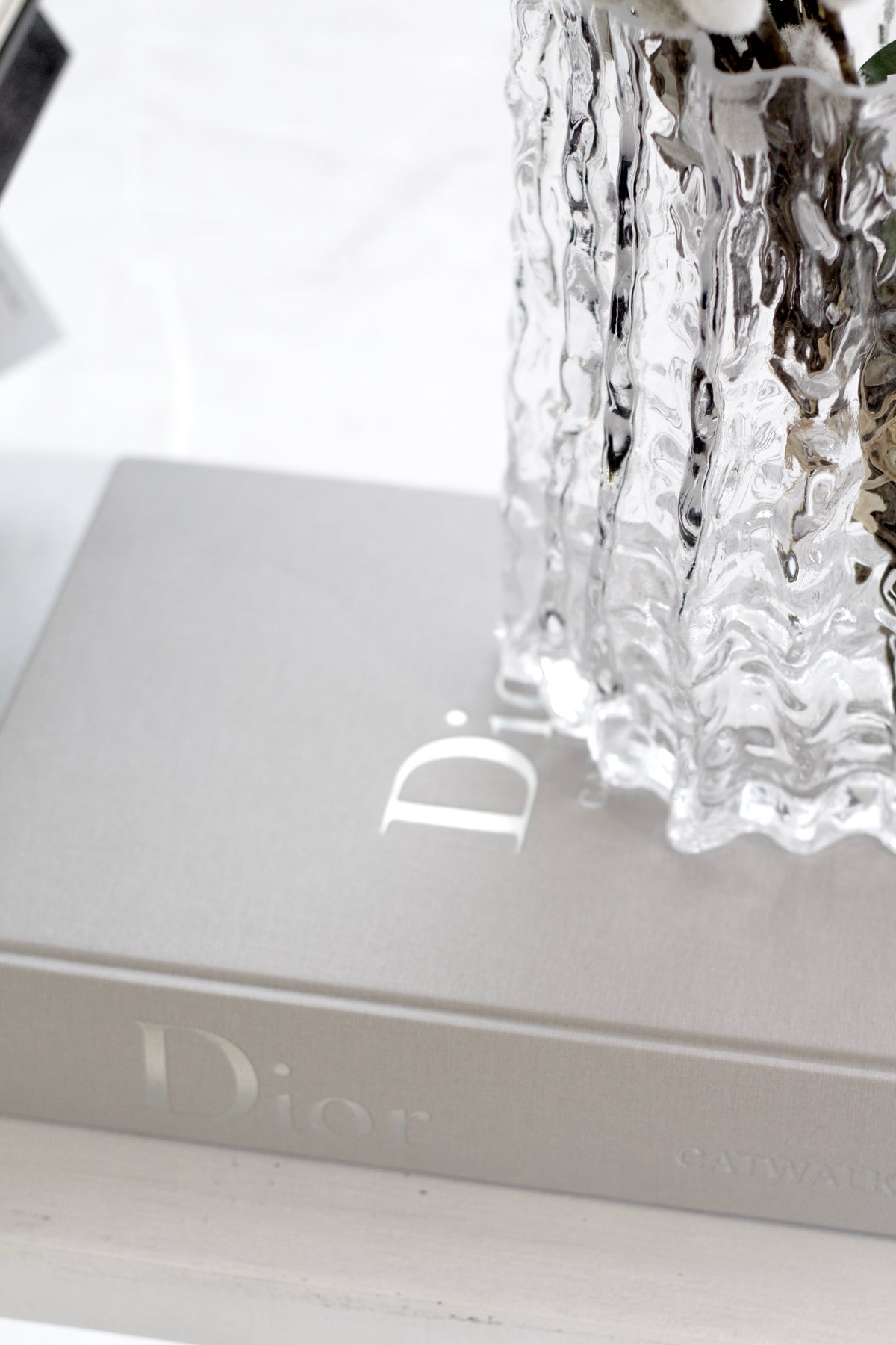 Clear Glacier vase of dried flowers on stacked books, framed close on the rippled base