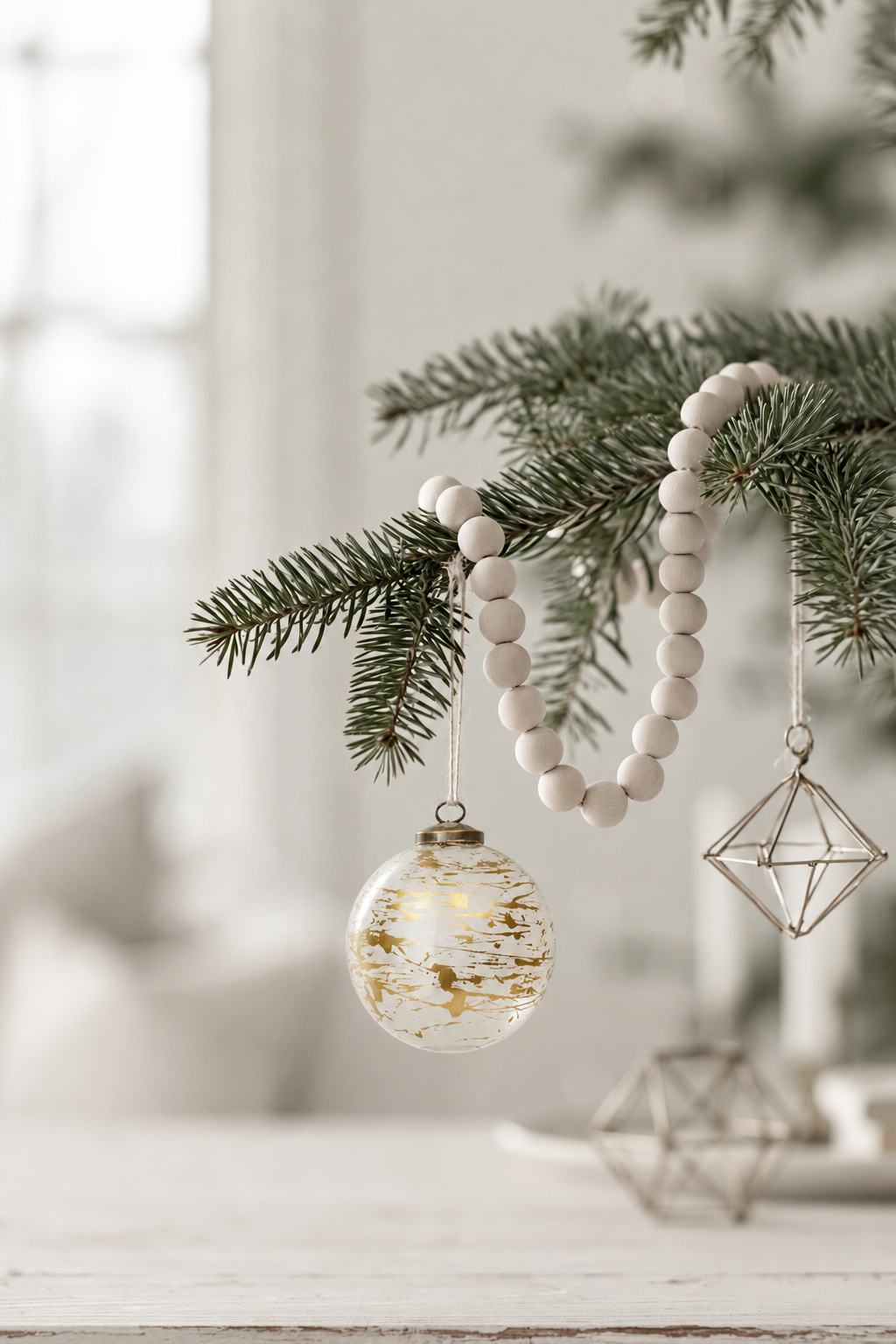 Gold Paint Splatter Glass Bauble 10cm hanging from a pine branch with a wooden bead garland and a geometric ornament