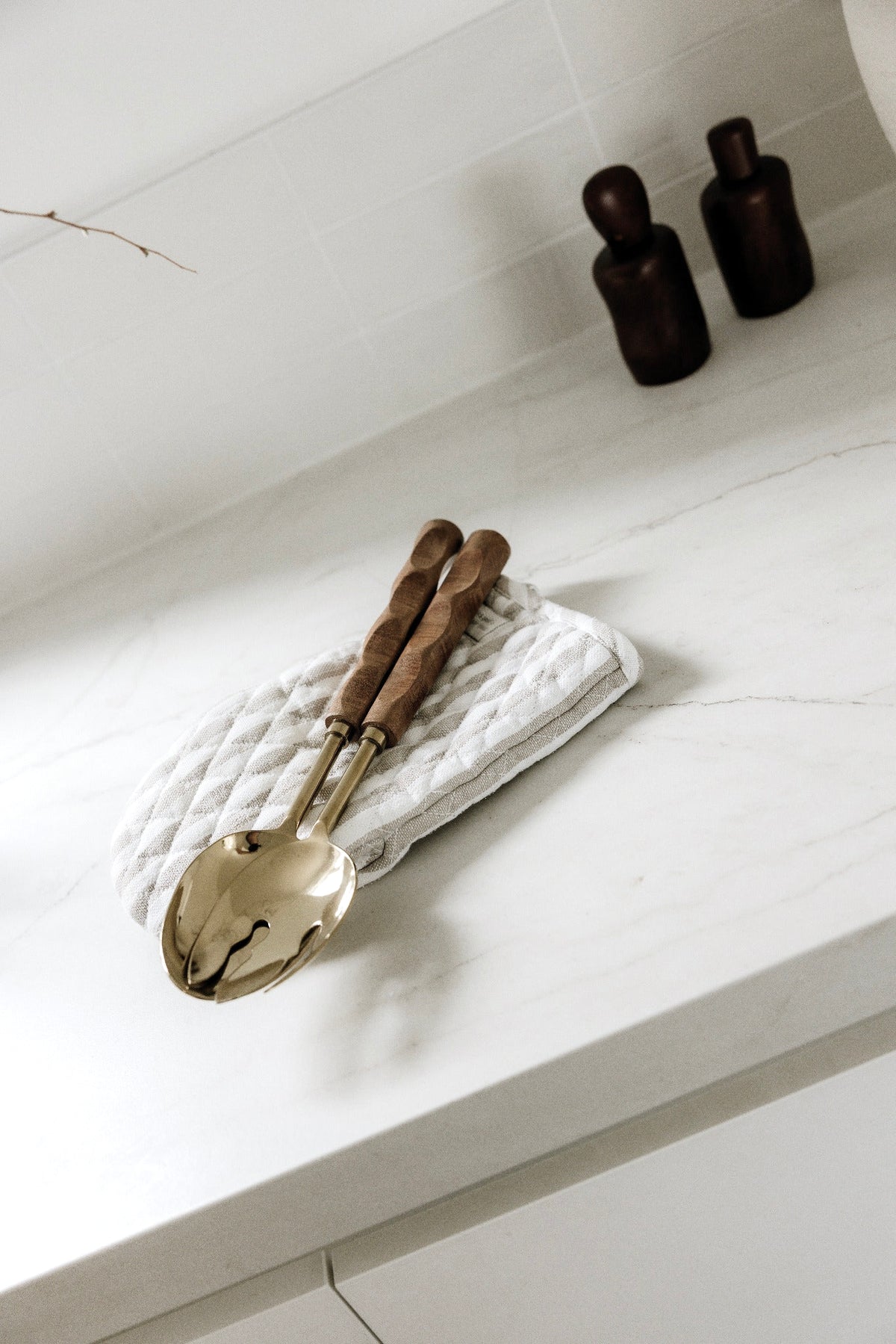 Gold and wood salad servers on a linen napkin on a stone bench beside dark wooden shakers