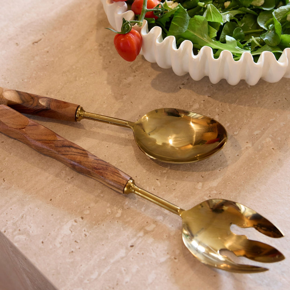 Gold and wood salad servers styled on a dining table with serving bowls
