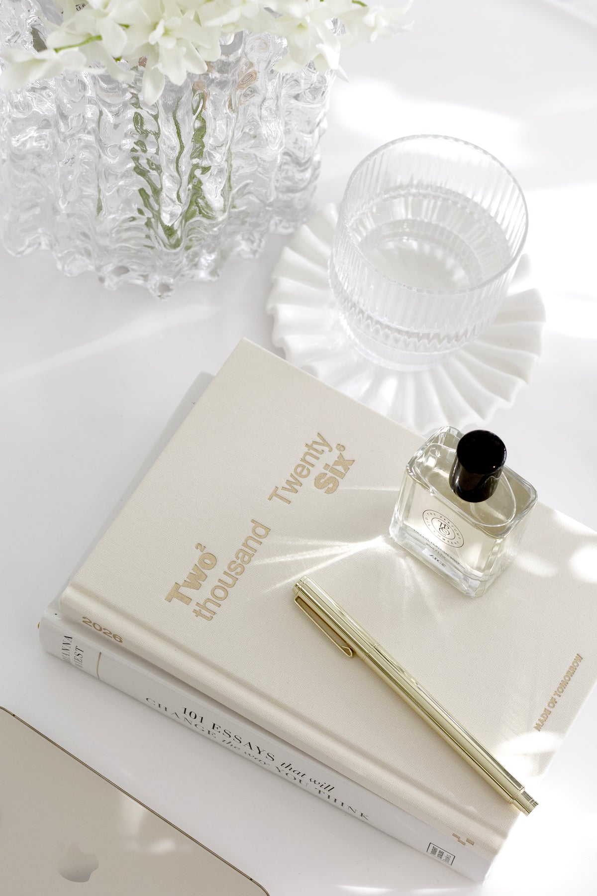 Golden refillable metal rollerball pen styled on a neutral journal stack with soft white decor and glassware.