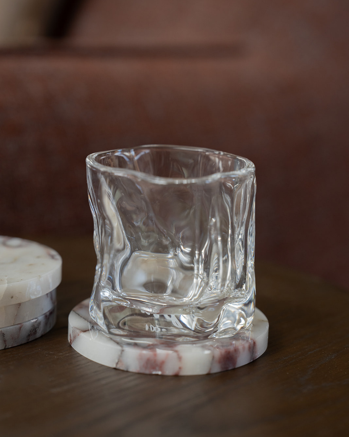 Clear rippled glass tumbler on a Viola Marble coaster with a small stack of coasters, on dark timber