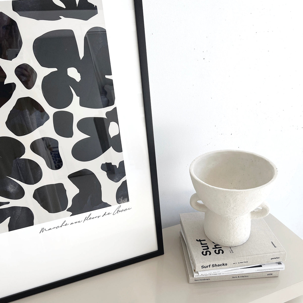 Close view of the Gucci Flower Market print in navy in a black frame beside a cream vase