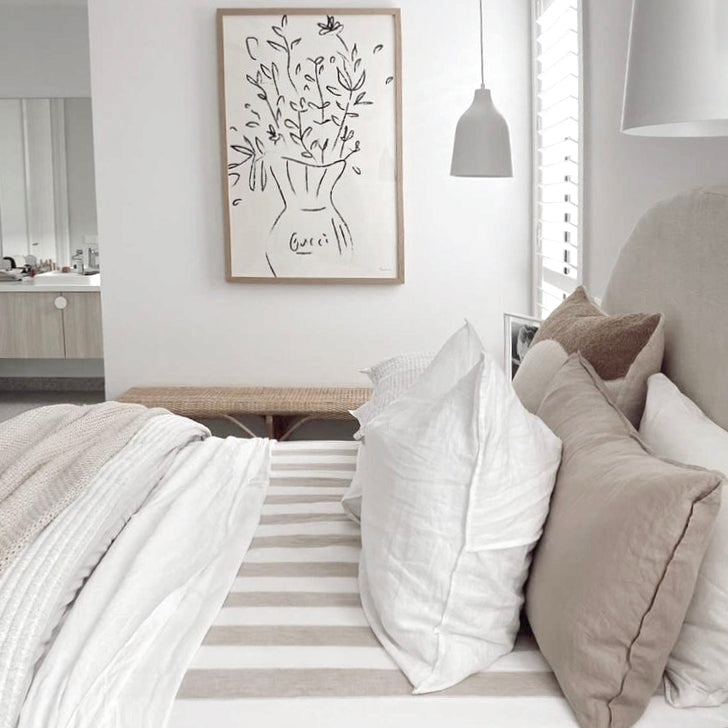 Gucci Flowers print in a natural frame above a bed with white and taupe linen