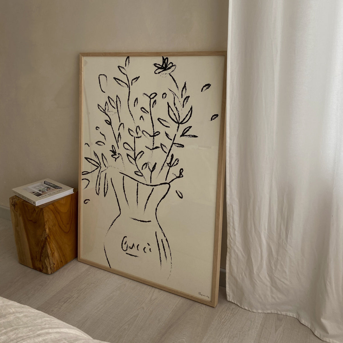 Gucci Flowers print in a natural frame leaning against a wall beside a timber stool