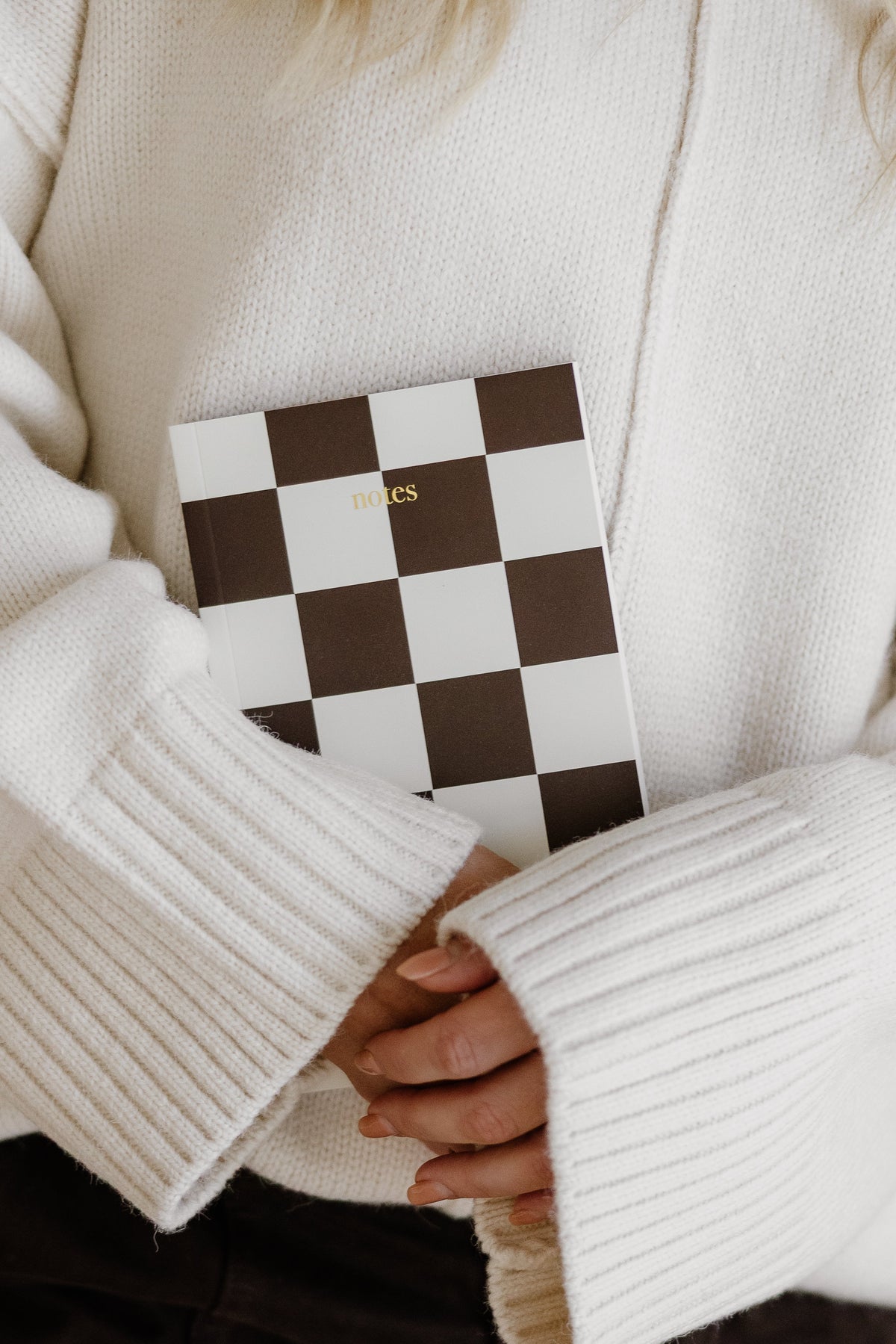 Person in a cream knit holding the Harmony brown check notebook