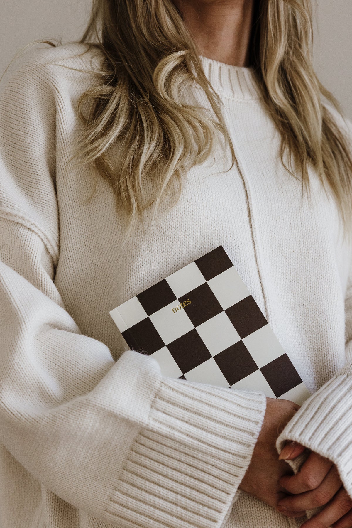 Close-up of the Harmony check notebook held against a cream knit jumper
