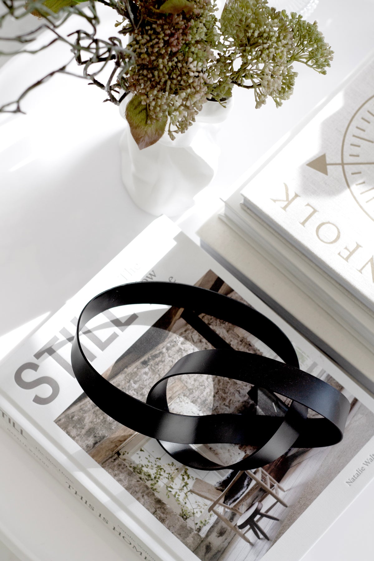 Black infinity loop metal sculpture styled on coffee table books in minimalist neutral interior