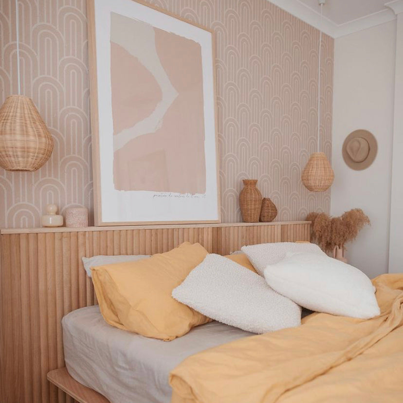 Ink print in pink framed above a timber bedhead with mustard and white bedding