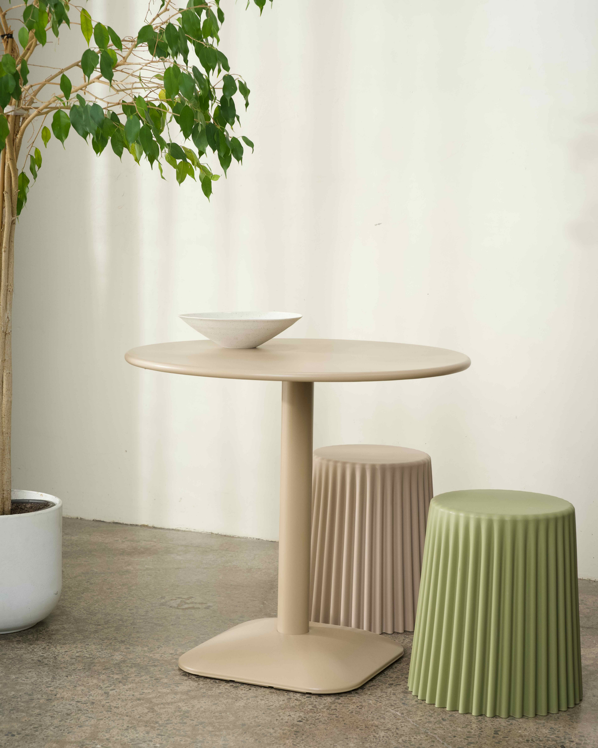 Nude Jasper Table with a speckled bowl, styled with two ribbed stools in nude and olive on a concrete floor