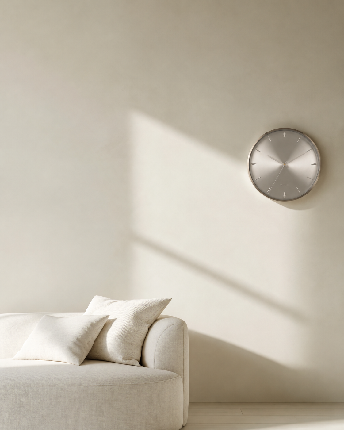 Jewel Wall Clock in silver on a warm white wall above a cream boucle sofa in afternoon sun