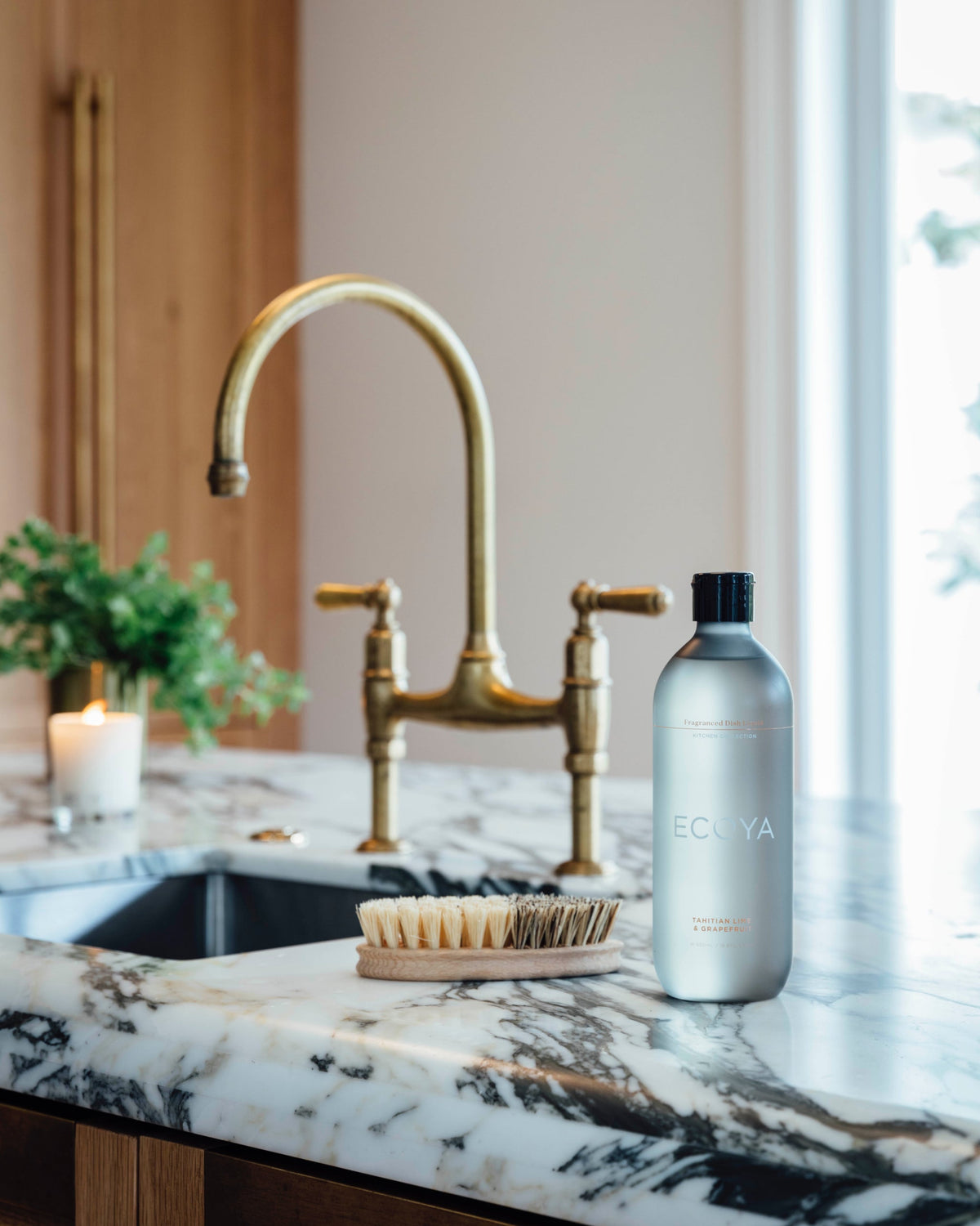 Ecoya dish liquid beside a brass tap and scrubbing brush on a marble benchtop