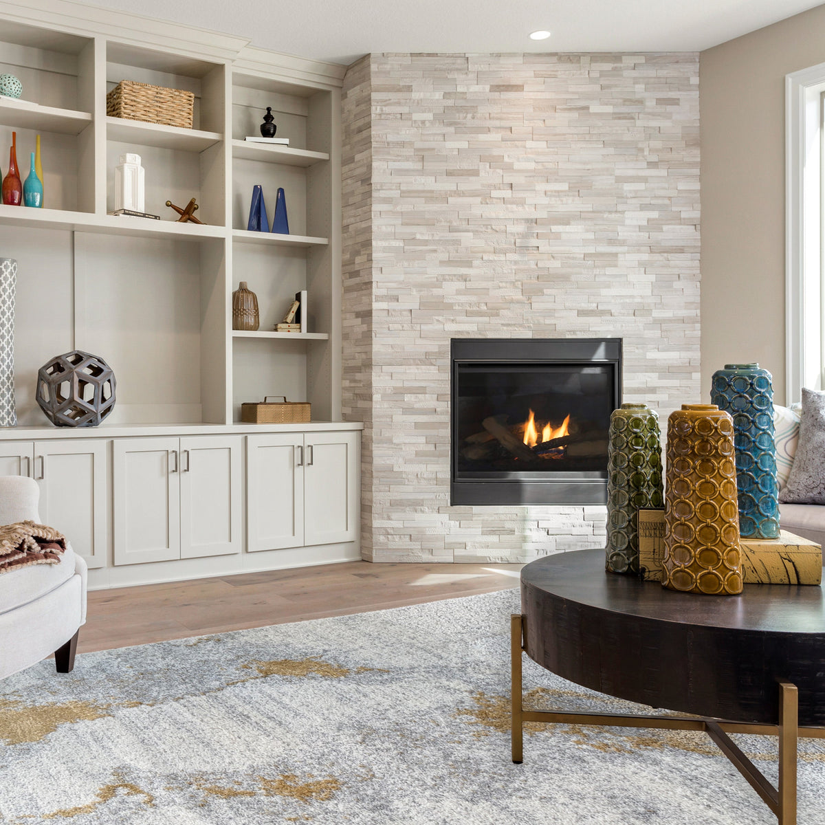 Grey and gold rug in front of a stone fireplace with built in shelving and a dark round coffee table