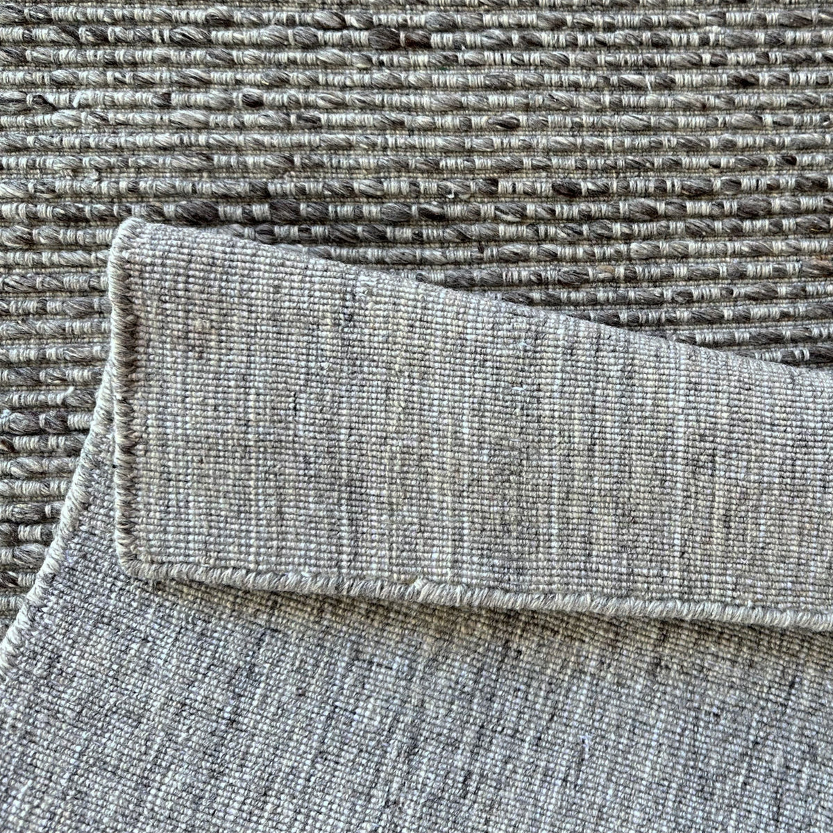 Grey ribbed rug folded over to show its woven backing
