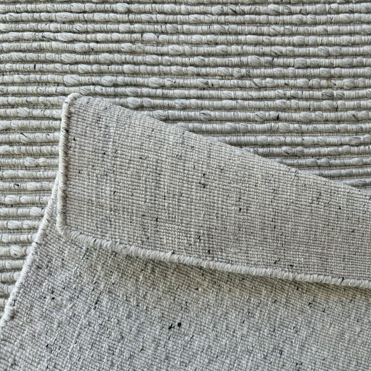 Light grey ribbed rug folded back to show the woven backing