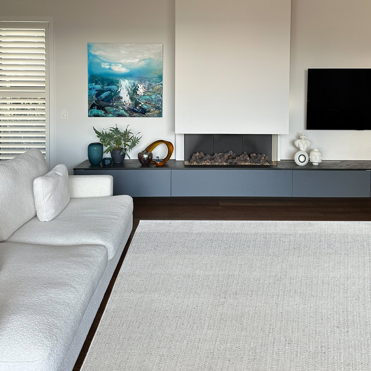 Light grey ribbed rug in a living room with a white sofa, a fireplace and a seascape painting