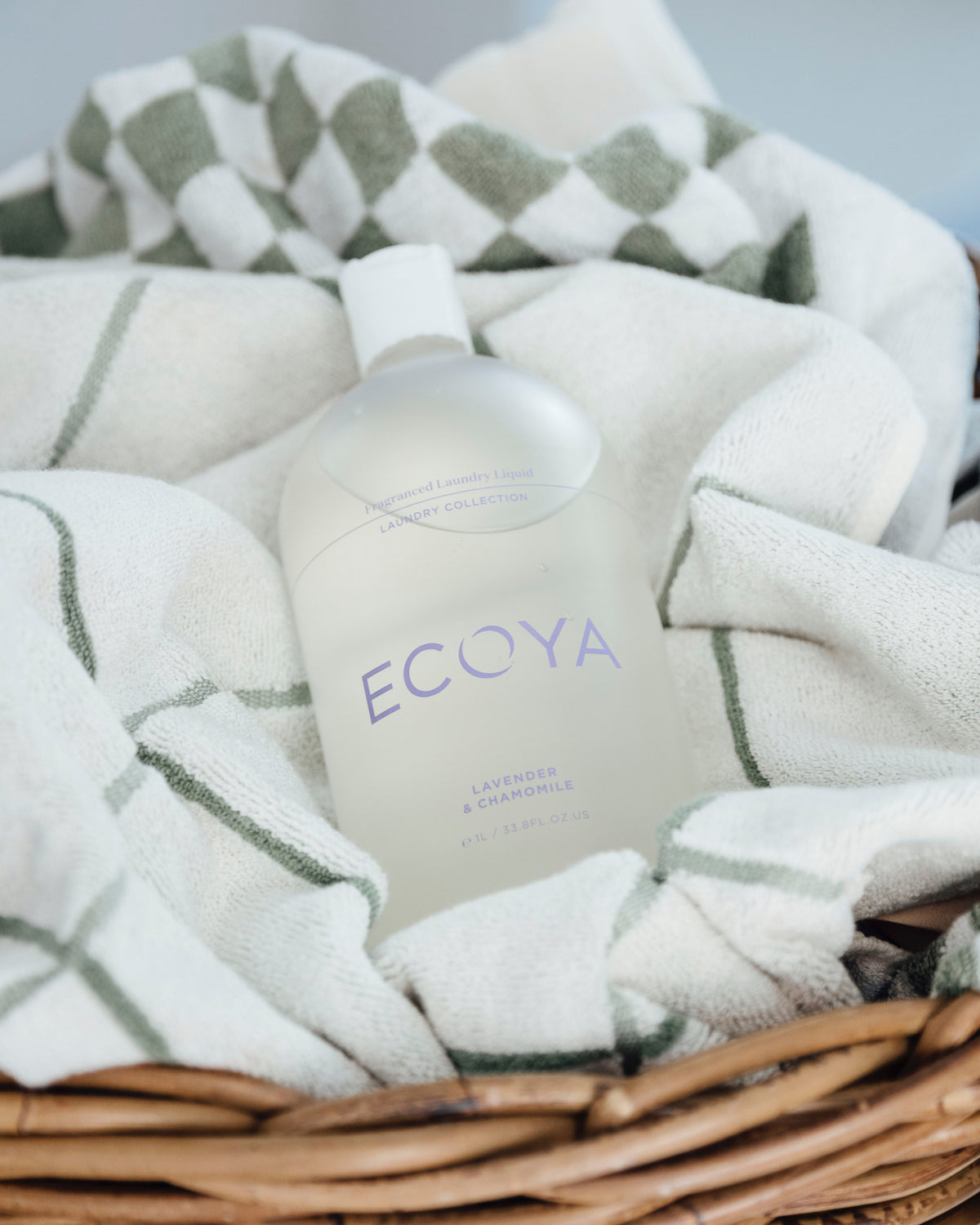 Ecoya Lavender and Chamomile laundry liquid resting on folded cream and sage checked towels
