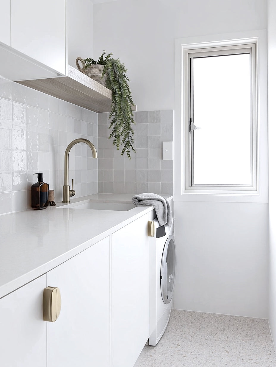Trailing eucalyptus in a woven basket on a timber laundry shelf above a white benchtop and brass tap