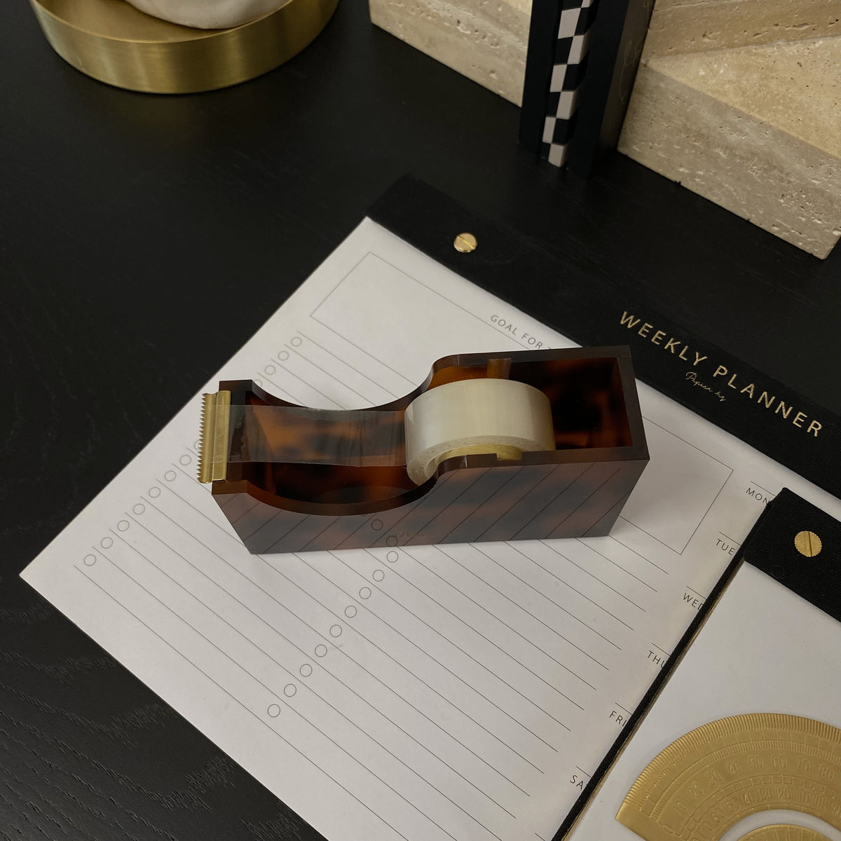 Tortoiseshell tape dispenser with a roll of tape on a black desk beside notepads