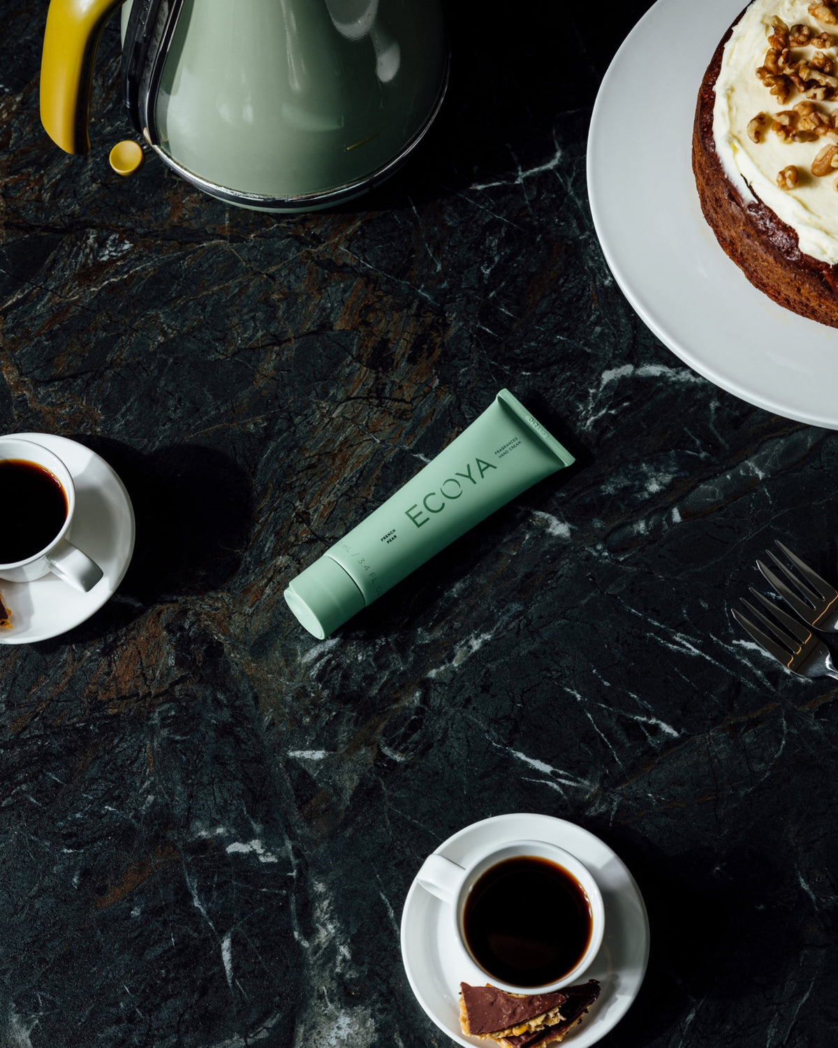 Green Ecoya hand cream tube on dark marble beside a cup of coffee