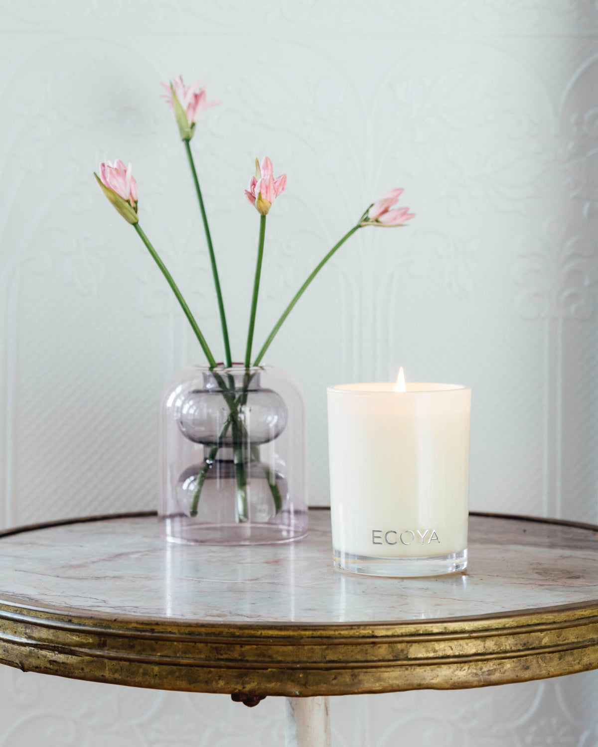 Ecoya Madison candle on a mirrored side table beside pink tulips in a glass vase