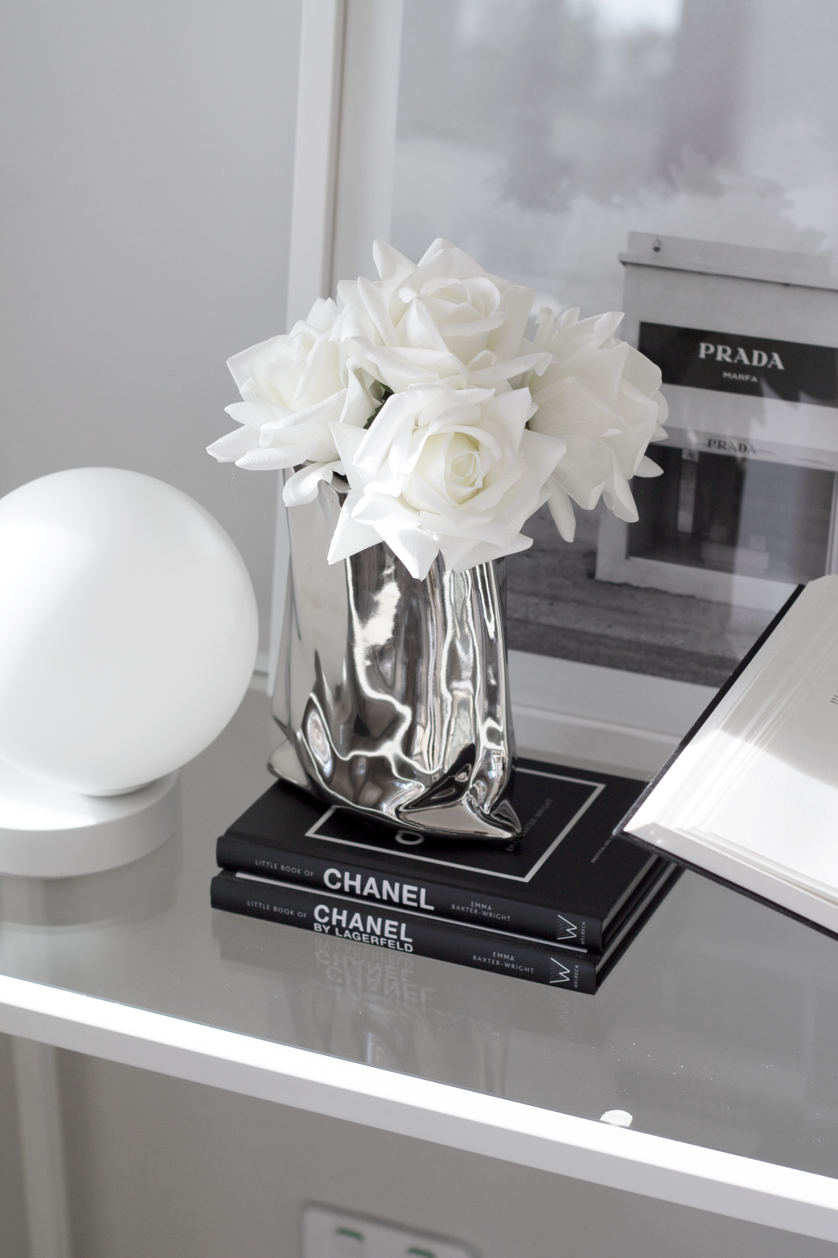 Little Book of Chanel by Lagerfeld hardback styled on a glossy console with a silver vase and white roses.