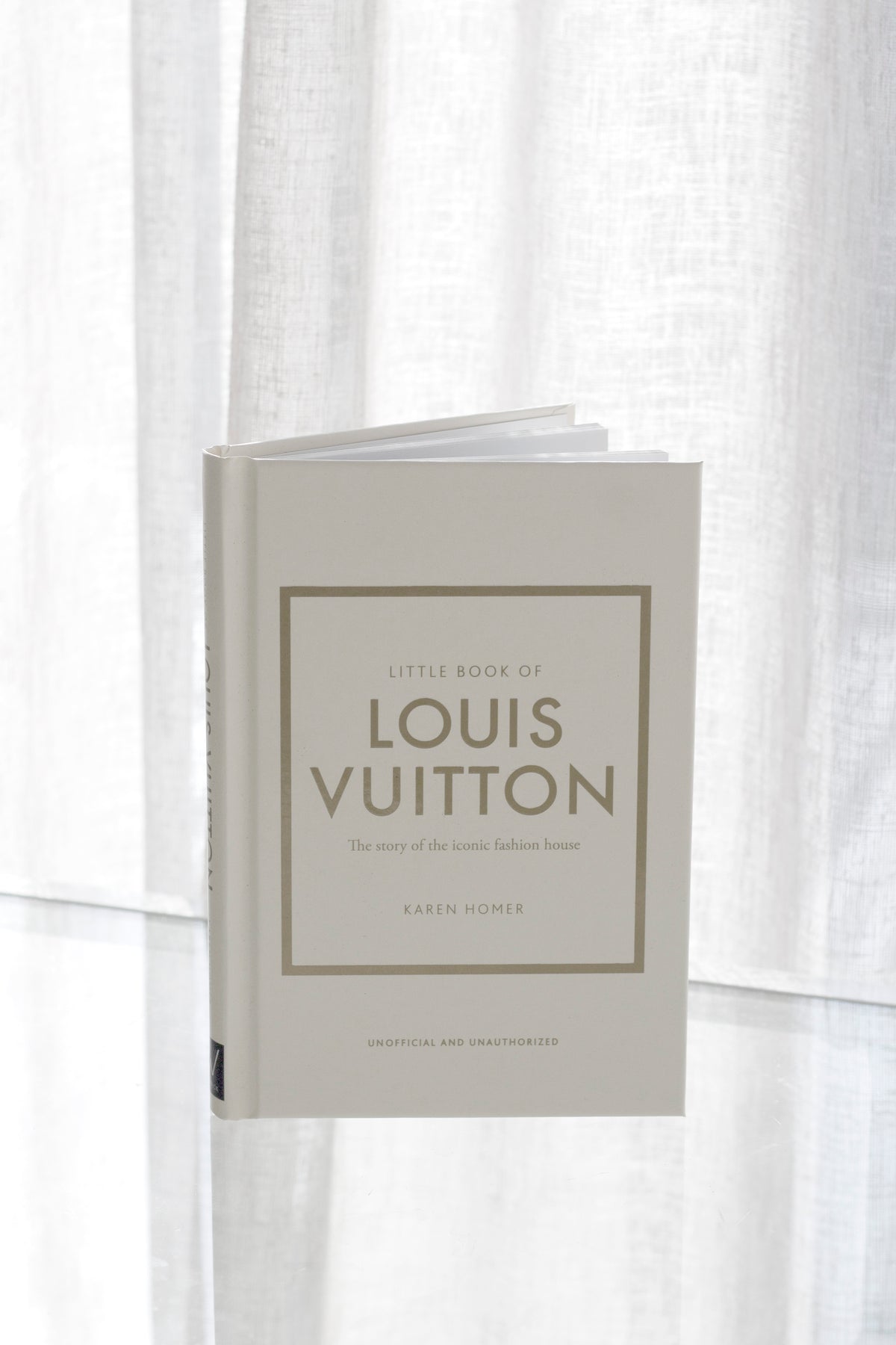Little Book of Louis Vuitton standing upright against soft sheer curtains in minimal natural light.