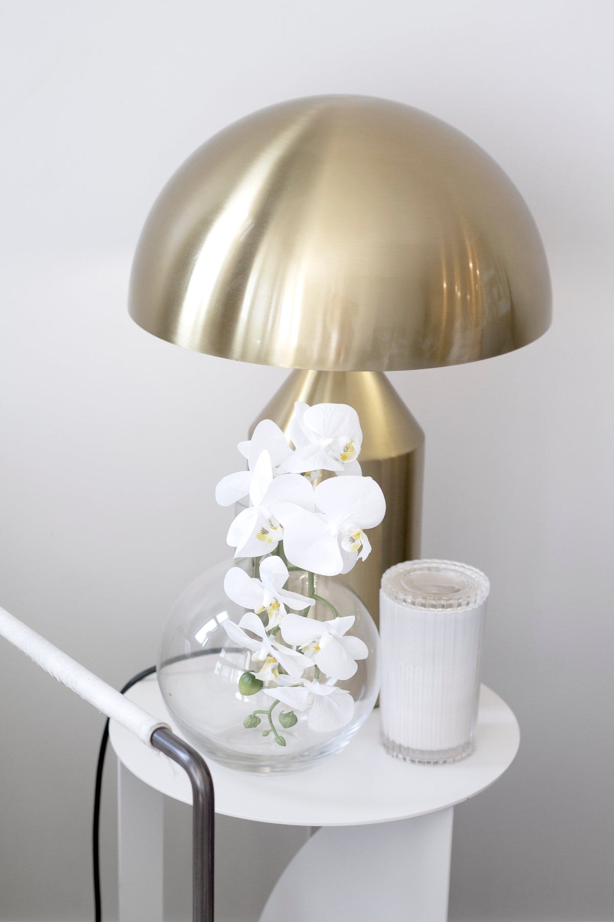 Brass dome lamp beside white orchids and a fluted candle on a small white side table
